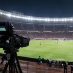 Hak Siar Liga Indonesia: Siapa Pemegangnya dan Cara Menonton Kamera siaran mengarah ke pertandingan sepak bola di stadion Indonesia dengan penonton di latar belakang