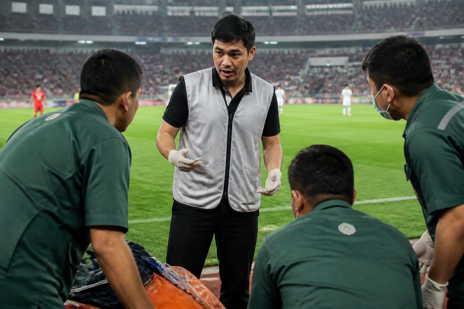 Medical officer berkoordinasi dengan tim medis di tepi lapangan stadion sepak bola