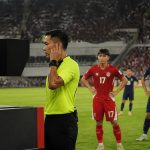 Wasit pertandingan sepak bola meninjau tayangan VAR di monitor tepi lapangan saat pemain menunggu di stadion
