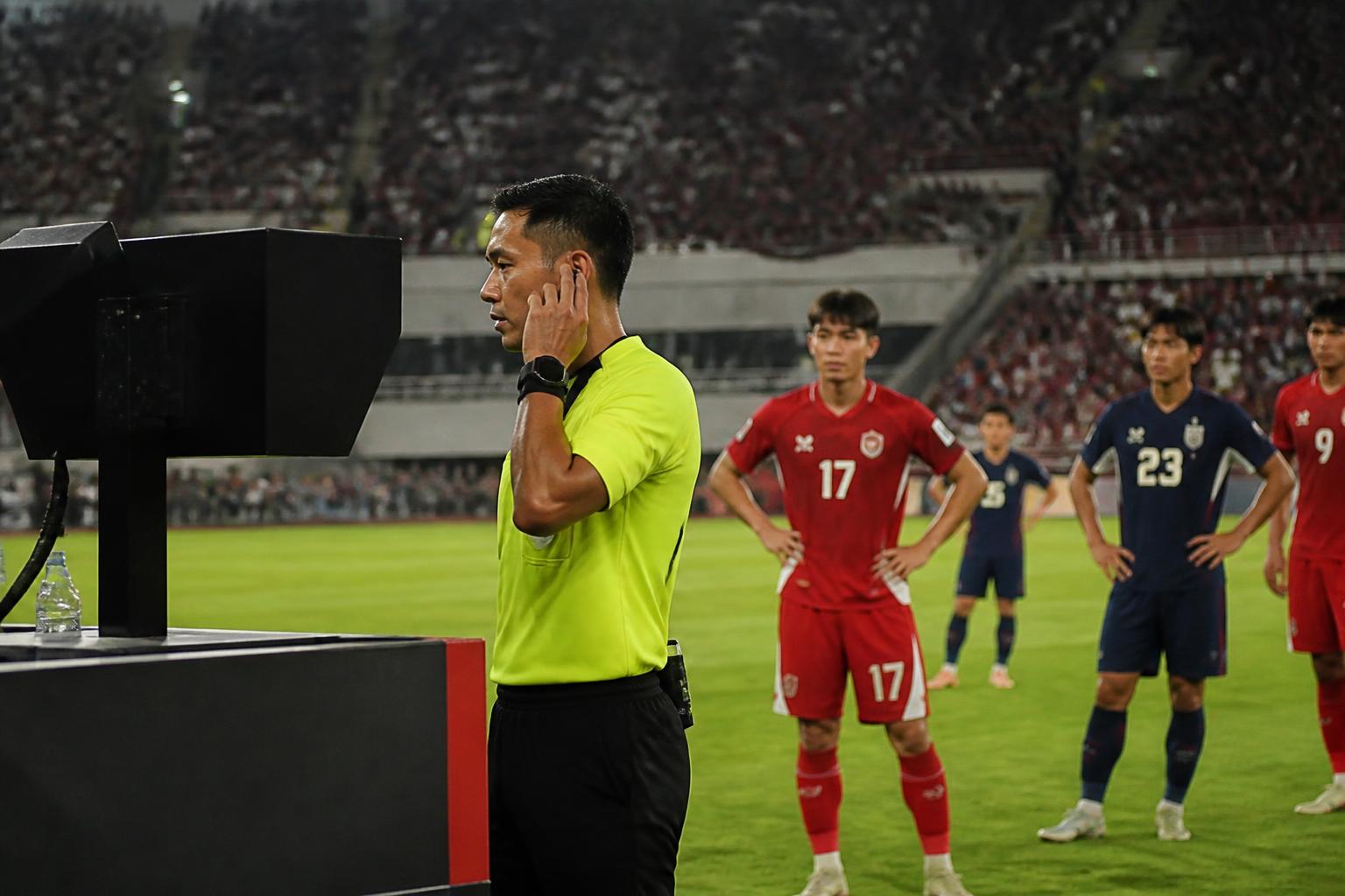 Wasit pertandingan sepak bola meninjau tayangan VAR di monitor tepi lapangan saat pemain menunggu di stadion