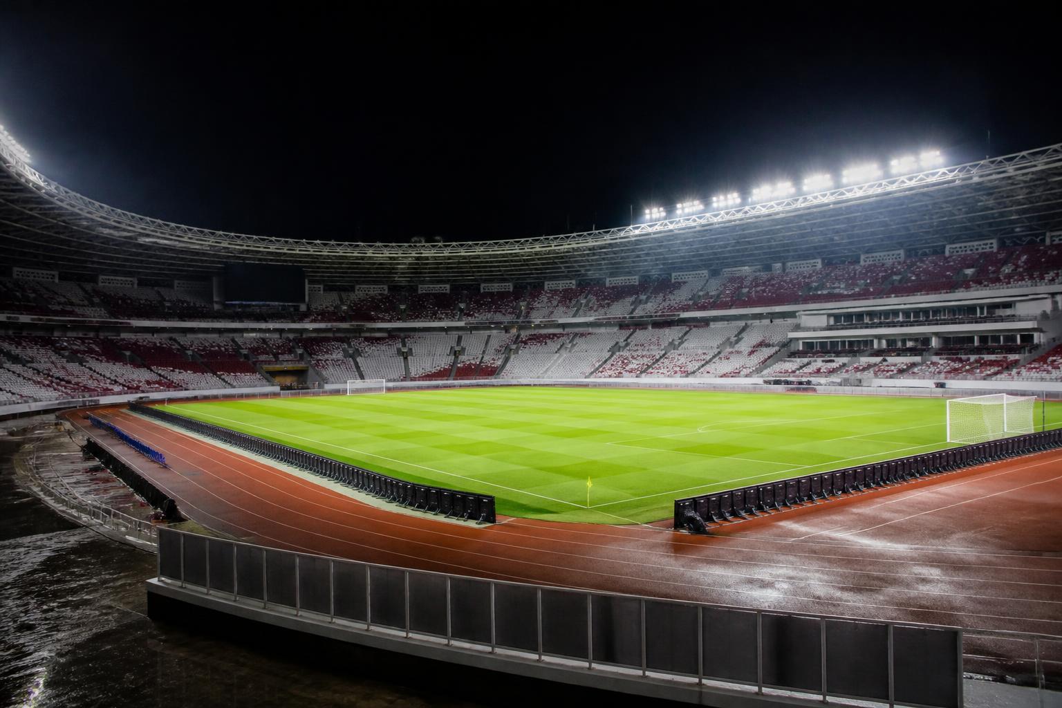 Lapangan stadion sepak bola Indonesia yang diterangi lampu untuk pertandingan malam dengan tribun dan area operasional yang tertata